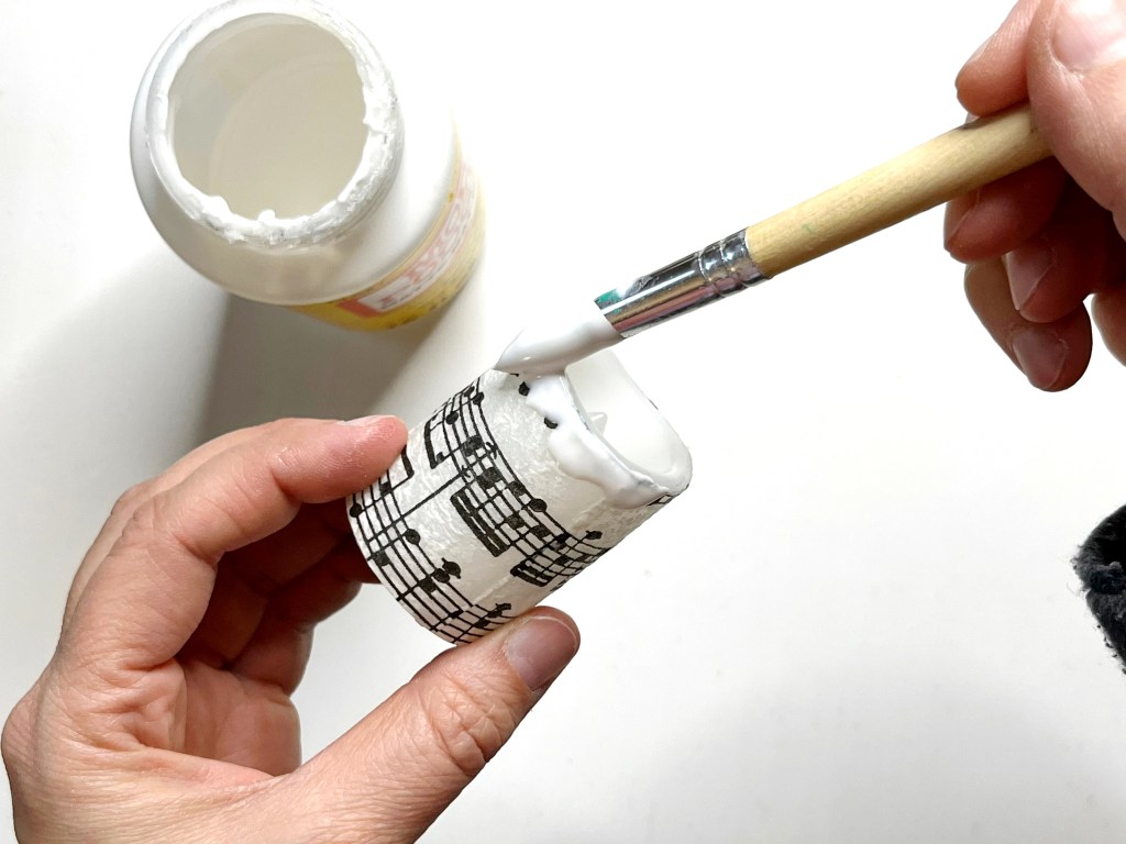 A paintbrush is used to apply a thick layer of Mod Podge (sealant glue) along the outer rim of the candle to imitate melted wax.