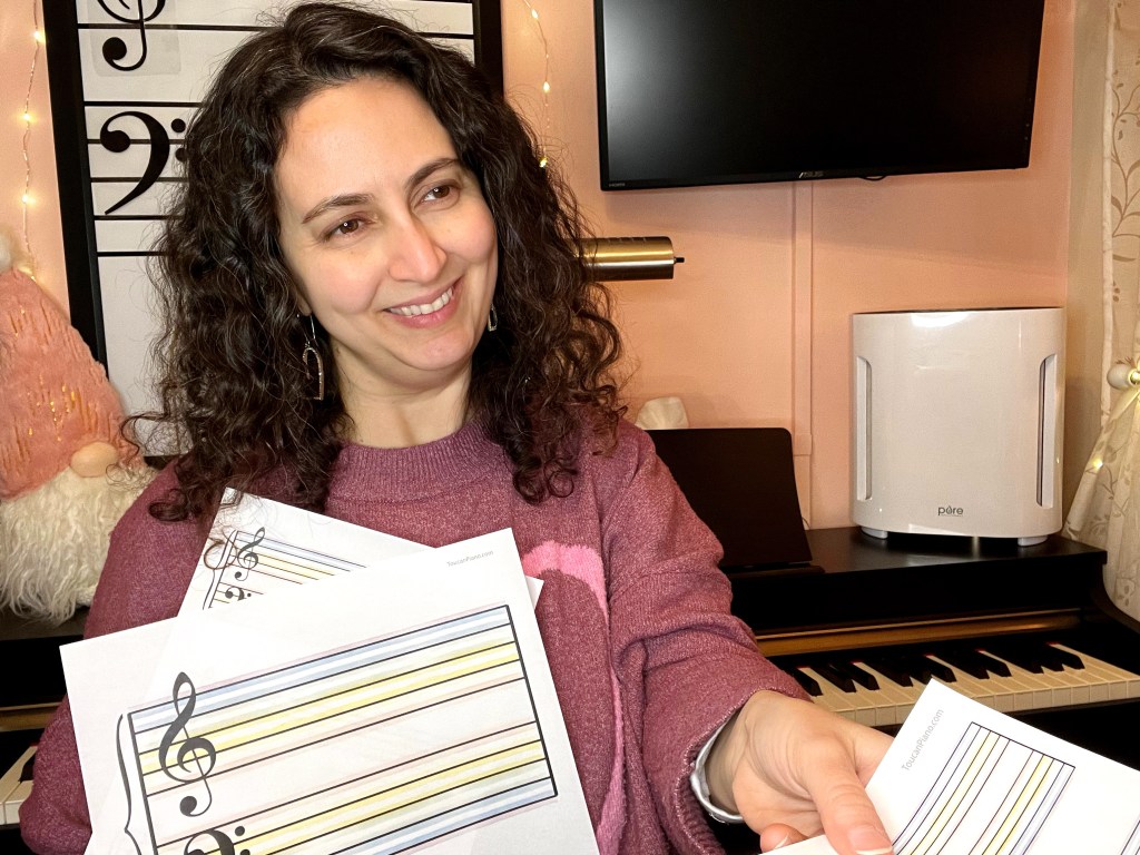 Piano teacher smiling while handing a student a sheet rainbow colored manuscript paper
