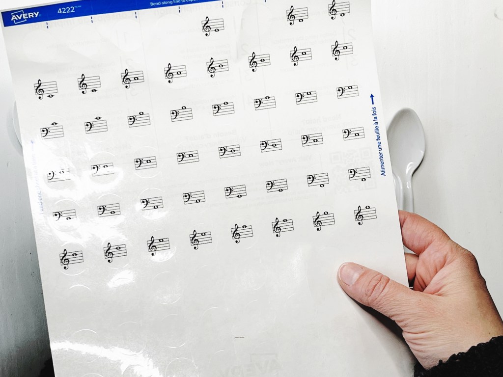 A hand holds a printed glossy white label sheet with musical notes on it.