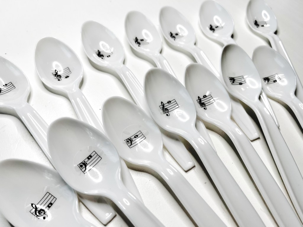 White plastic spoons with with music notes written on them sit neatly arranged in two overlapping rows.