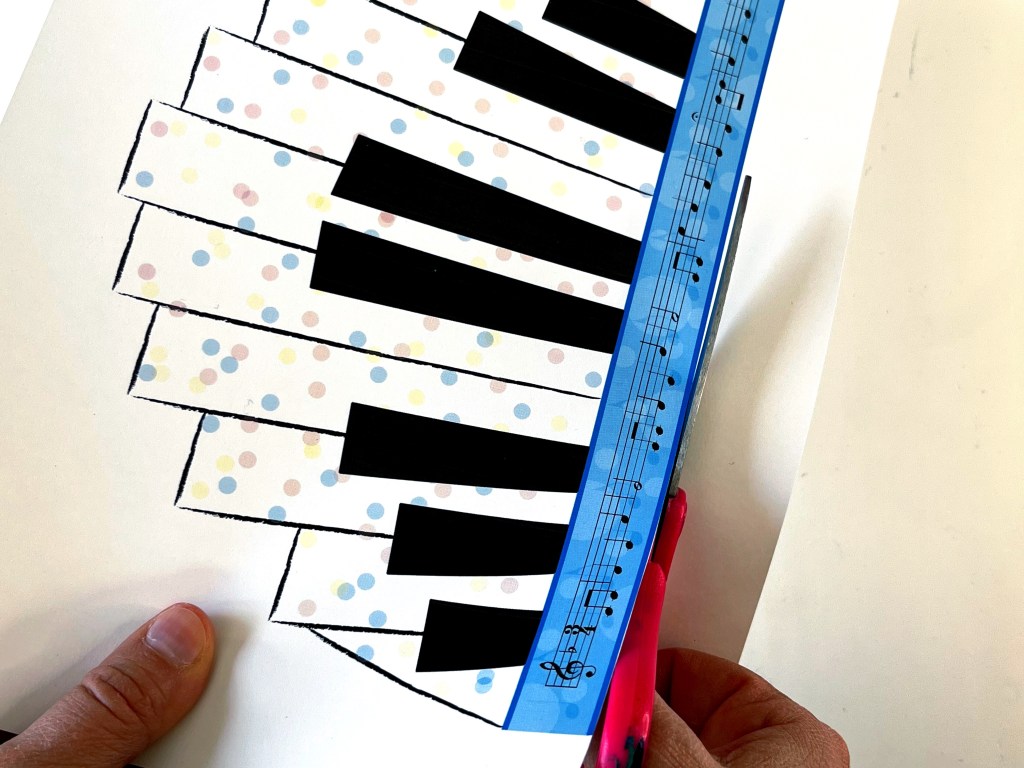 The piano birthday crown printout is being is cut out using the scissors.