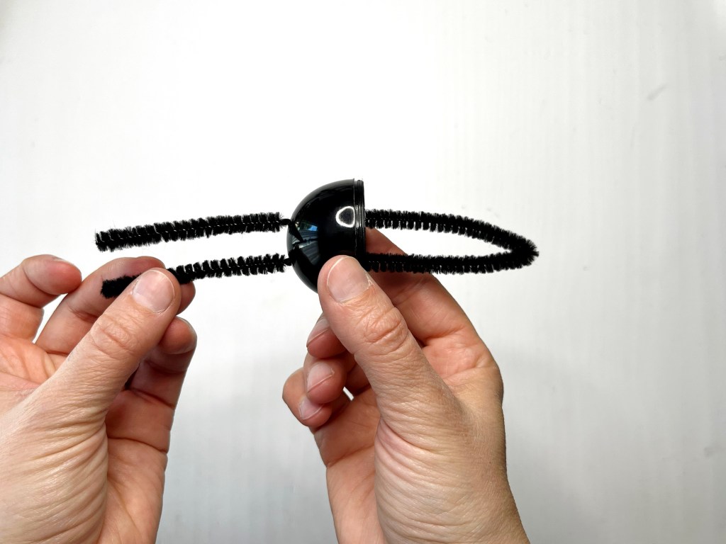 A black pipe cleaner is threaded through the holes in the bottom of a black plastic egg