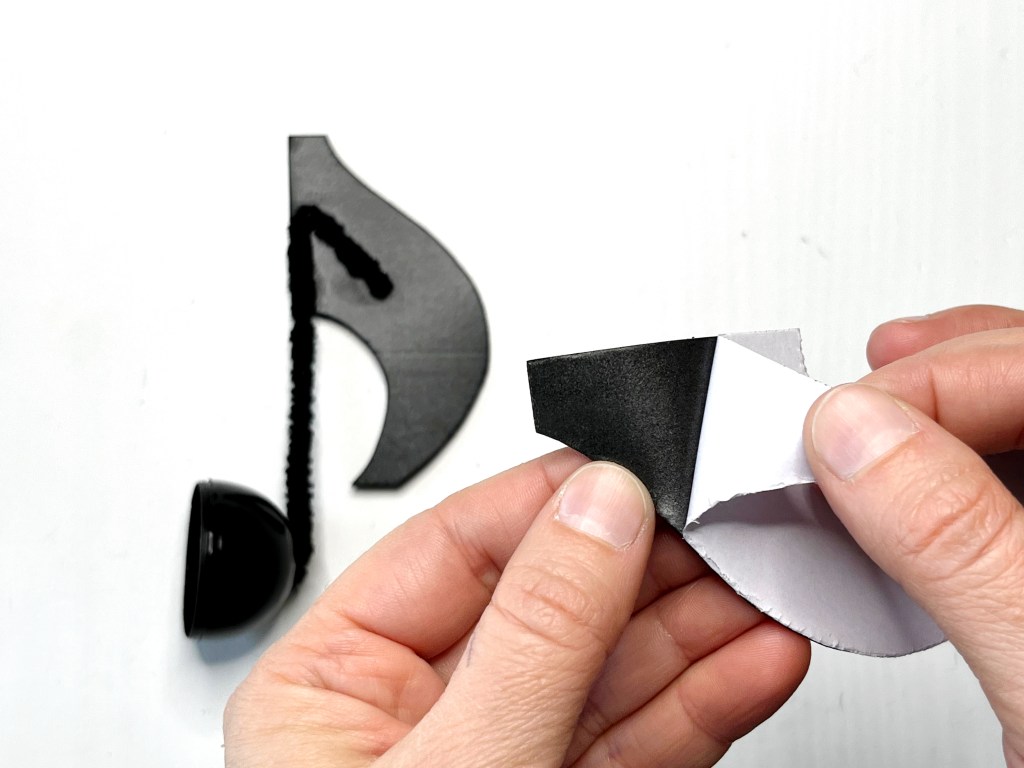 Hand peels the white paper backing off of a second black self adhesive craft foam