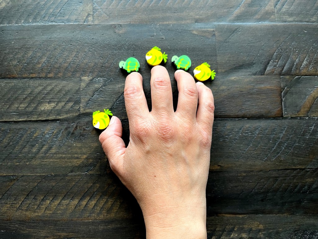 A hand sits on a table with five erasers placed in front of each finger.