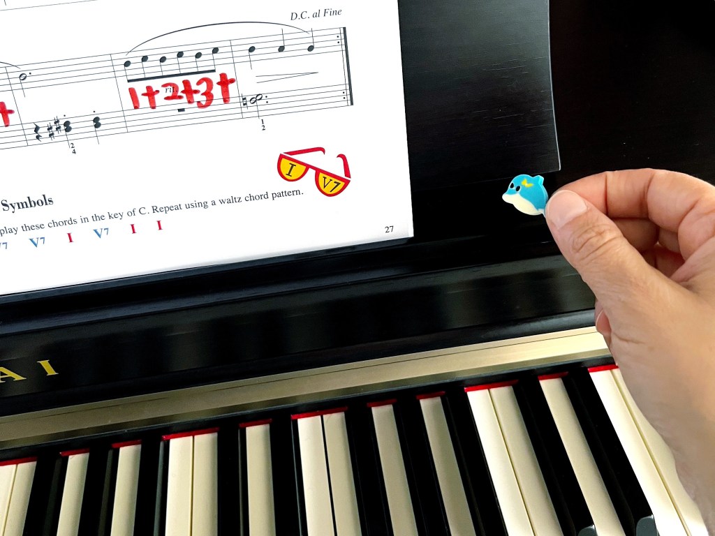A blue dolphin mini-eraser is moved to the right side of some sheet music on the piano.