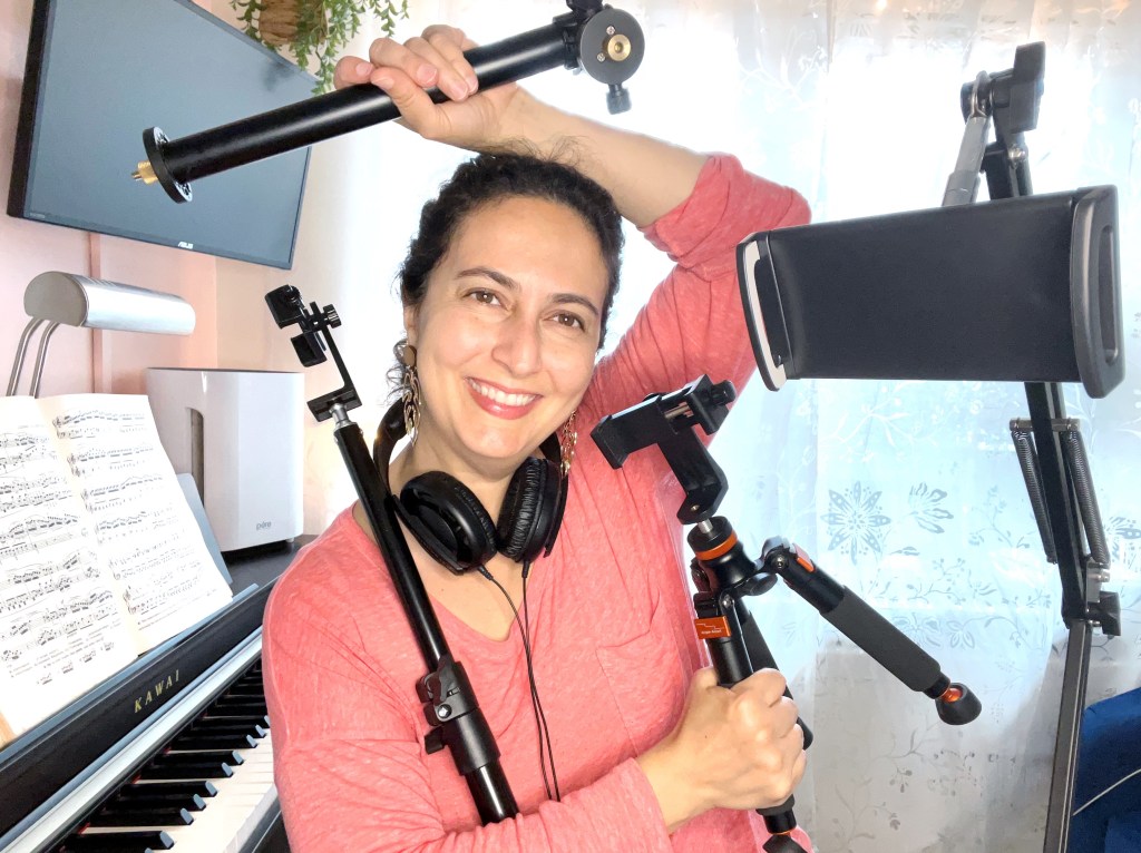 Dark haired woman in a pink sweater holds a variety of videography equipment