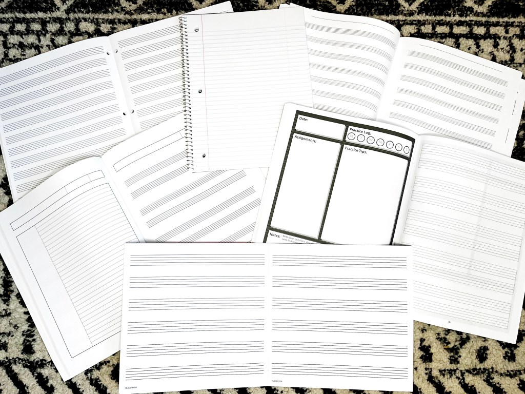 Manuscript notebooks and practice journals lay open on the a black and white rug.