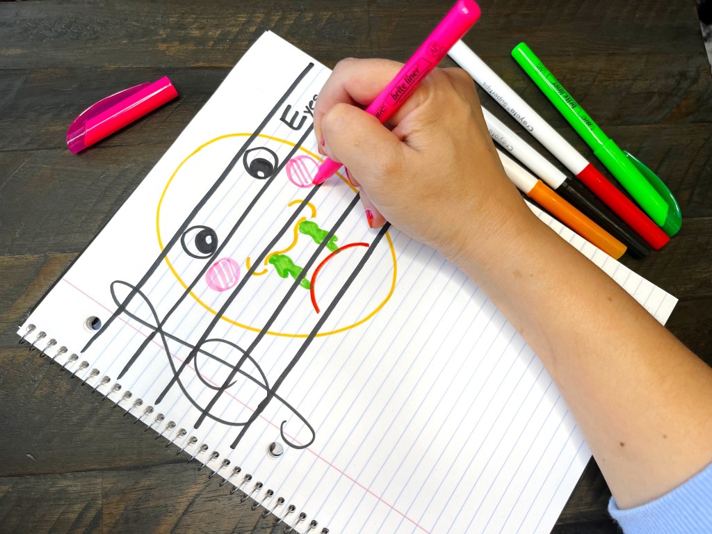 Piano teacher draws a boogery face on the treble staff in a composition notebook.