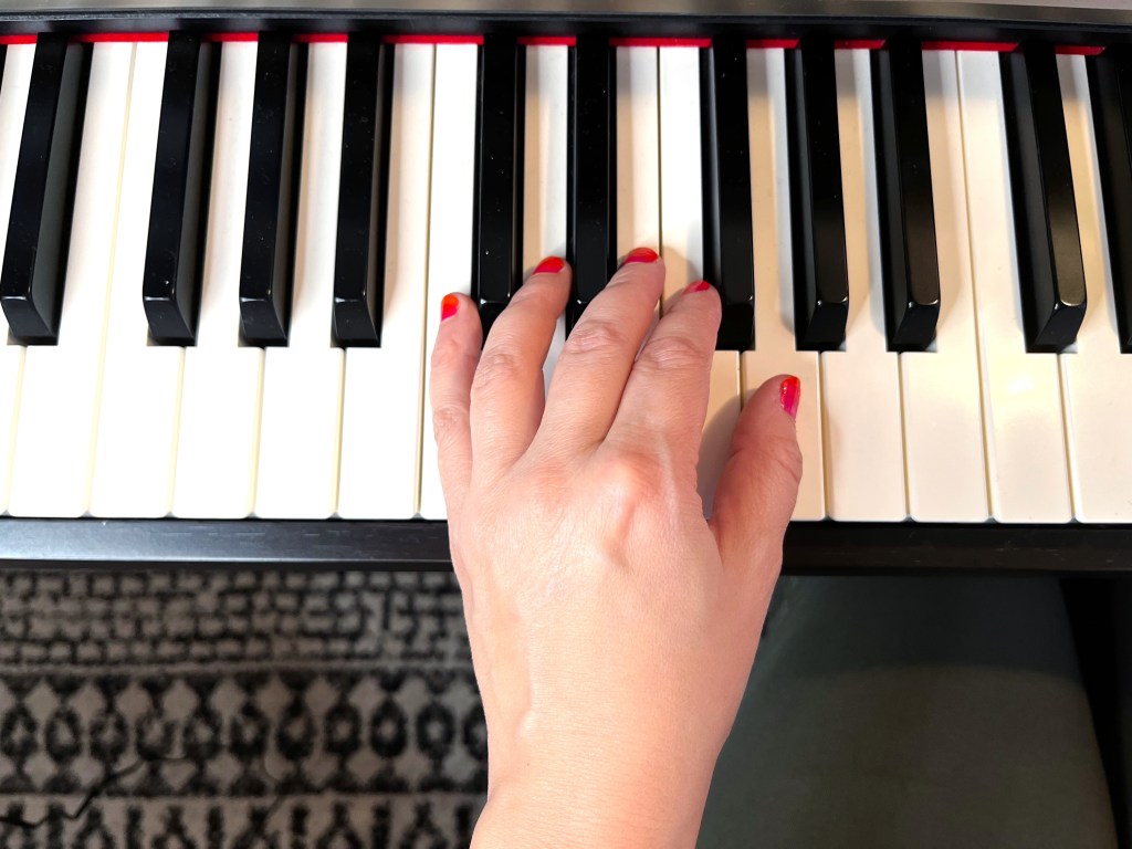 A hand sits on the piano with a bad hand posture which is forcing the pinky to sit on its side.