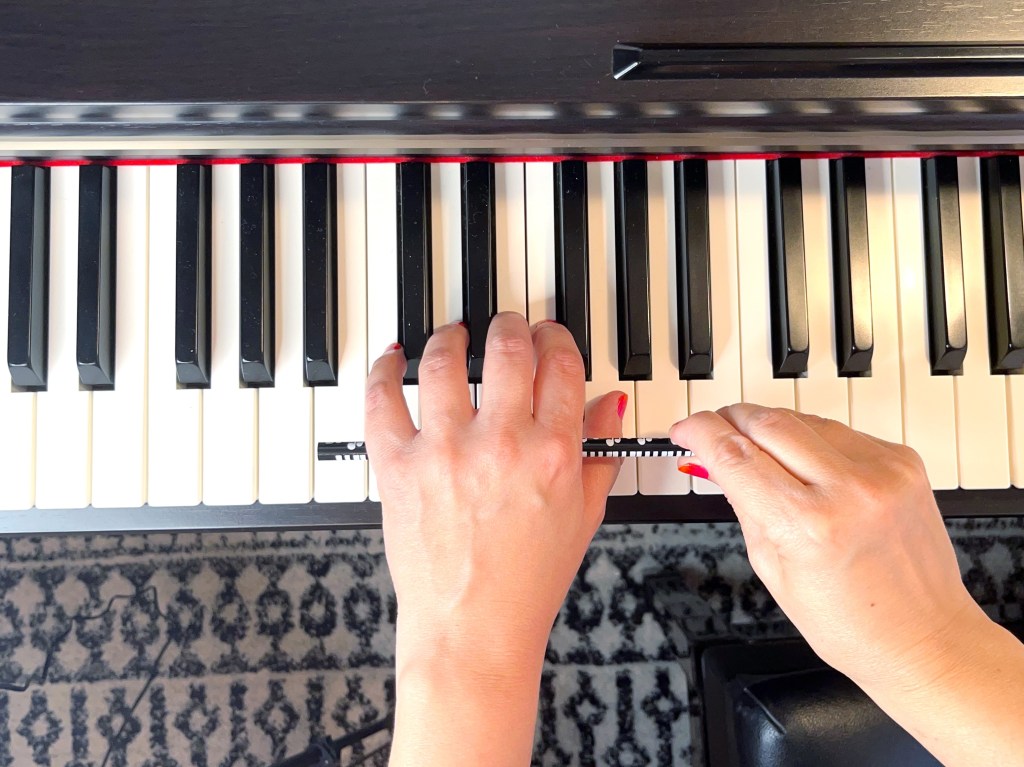 The right hand holds a pencil under the left hand to support the left hand so it can keep a proper posture at the piano.