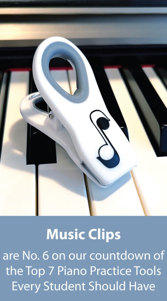 A white music clip with a gray rubber handle and decorated with a black and white eighth note sits on top of the keys of a piano.