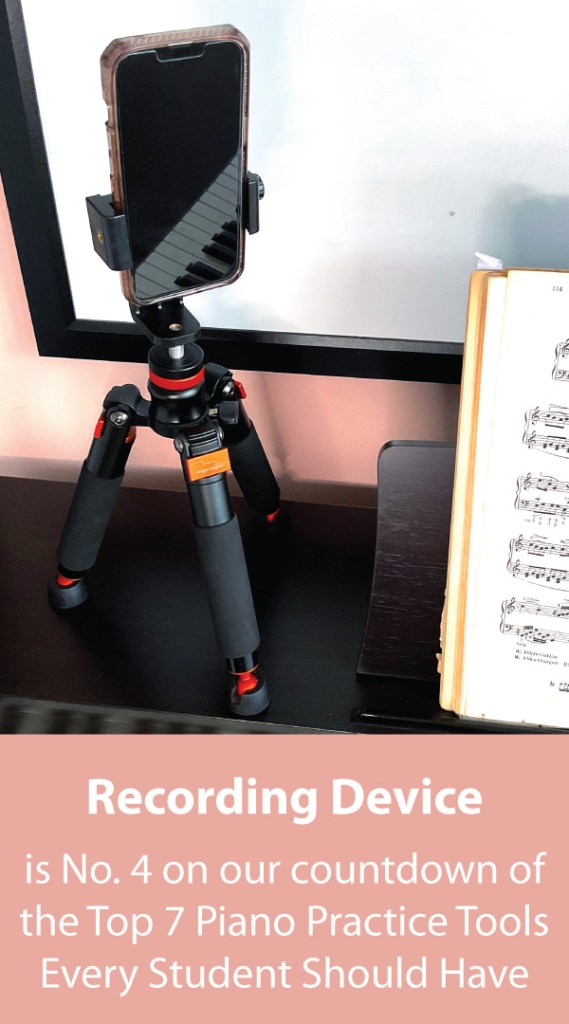 A smartphone connected to a tabletop tripod sits on top a piano next to some sheet music.