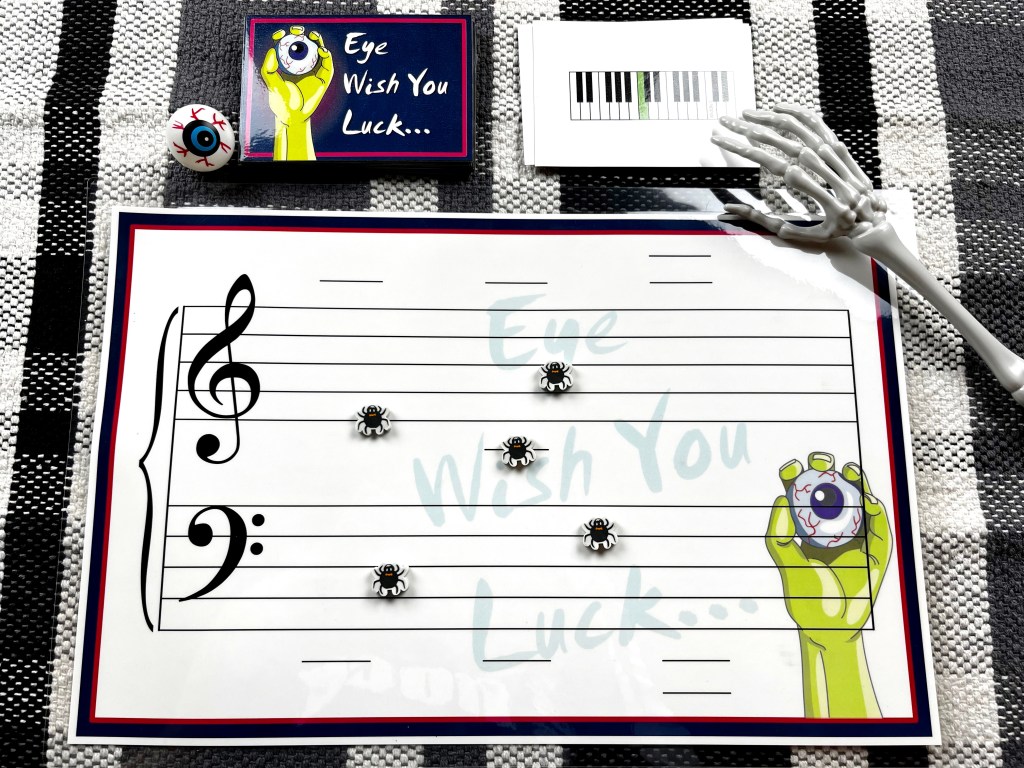 Eye Wish you Luck, the note-reading game, is set up on a black white and gray checked tablecloth. Spider erasers are used to mark note placement while a skeleton hand reaches for the next card.