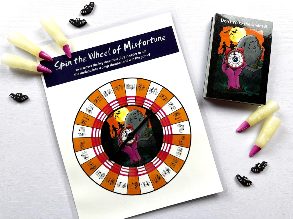 Don't wake the undead, a note-reading flashcard game, sits on a white table surrounded by zombie fingers and bats.