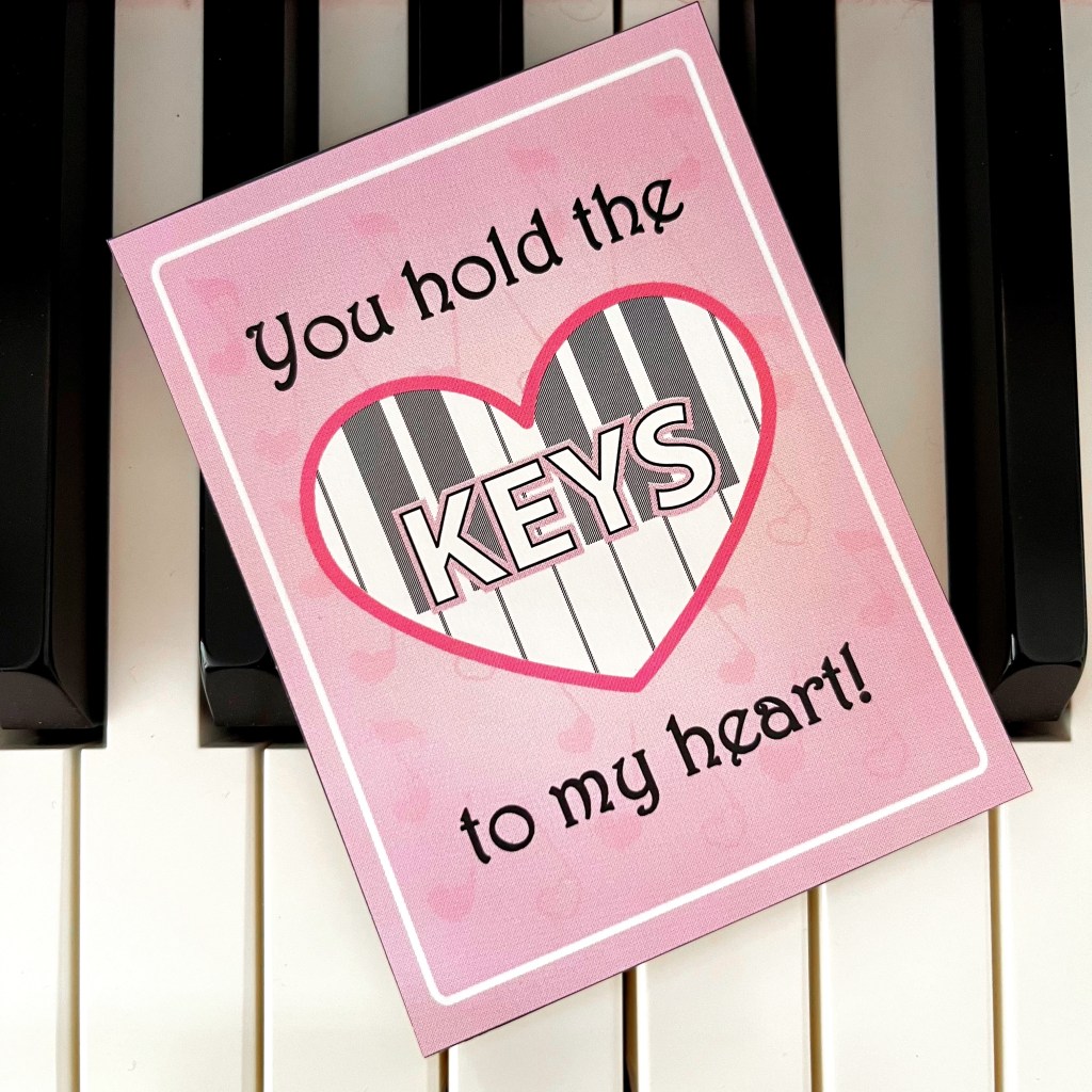 A pink Valentine's Day Card sits on top of the keys of a piano. They card reads "You hold the keys to my heart".