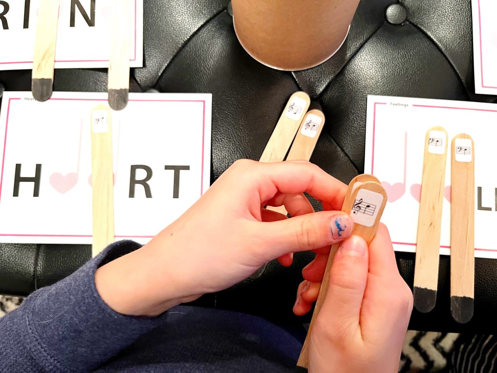 A piano student reads and sorts through popsicle sticks with music notes written on them trying to find a match for one of the Valentine's words.