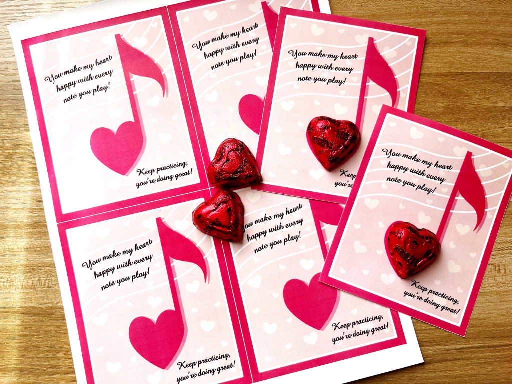 Music themed Valentines with heart shaped chocolates sitting on a wooden table.