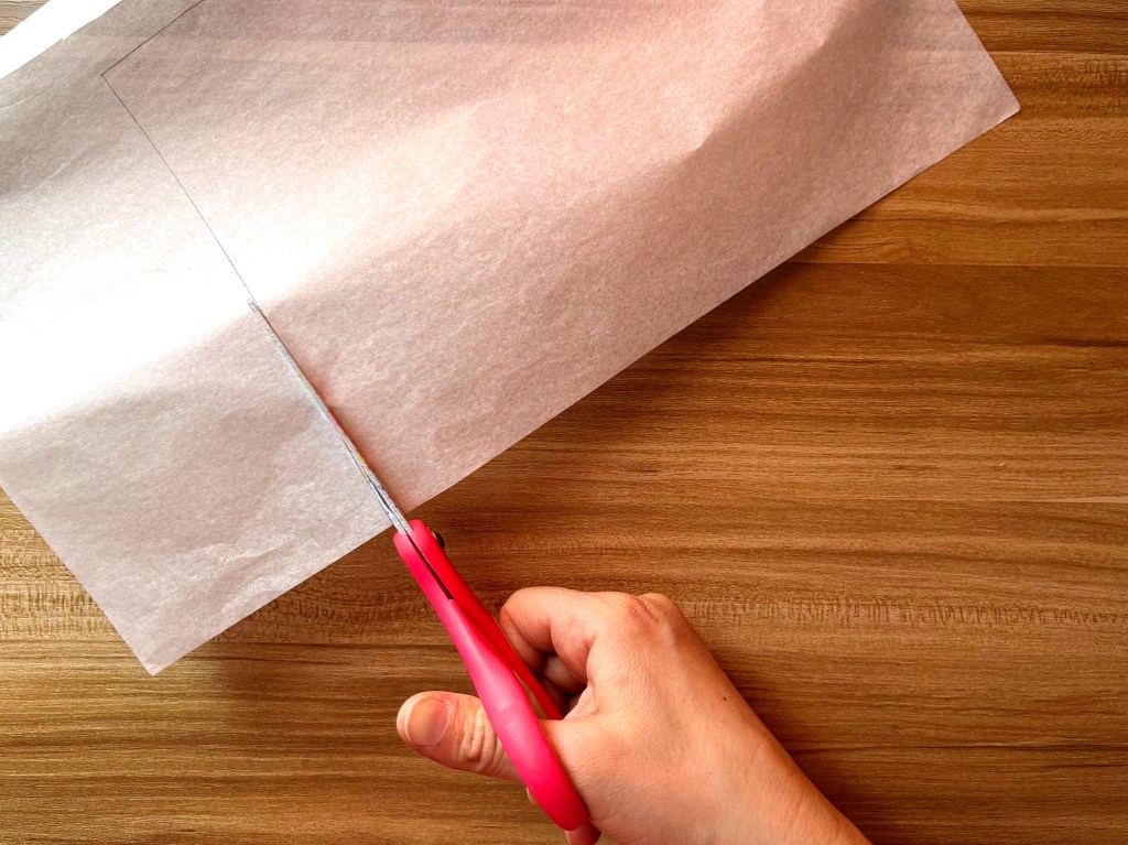 A person cuts a sheet of white tissue paper using a pair of pink scissors.