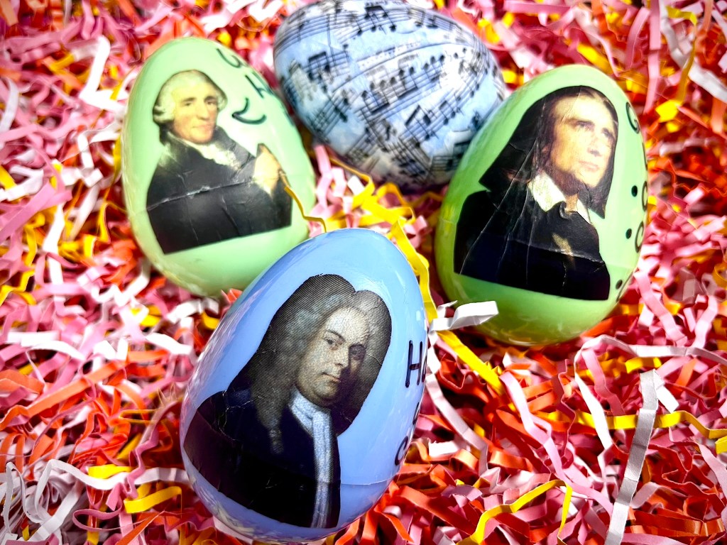 Four composer easter eggs with Haydn, Liszt and Handel sit in a pile of pink fake grass.