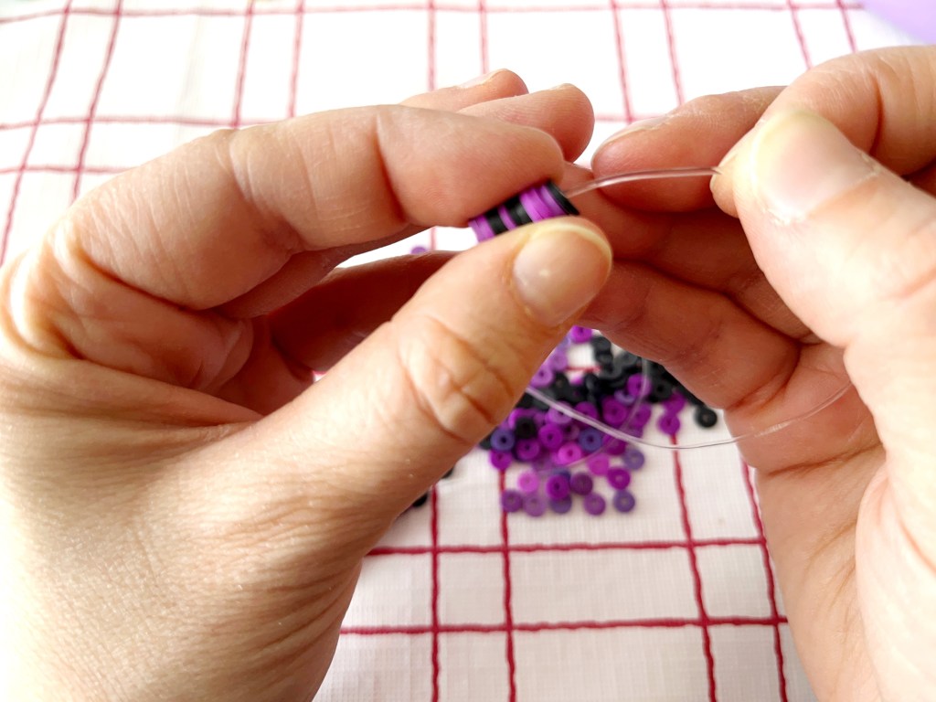 Purple and black polymer clay beads are strung onto an elastic stretch cord.