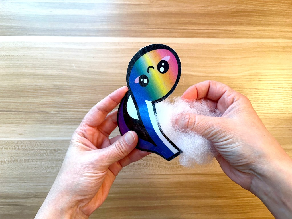 Stuffing a rainbow colored paper eighth note squishy with stuffed animal poly fill