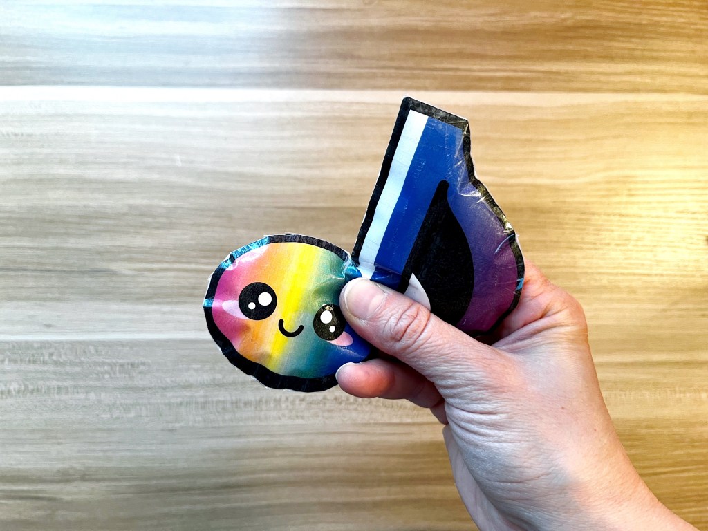 Rainbow colored eighth note paper squishy being squeezed by a hand