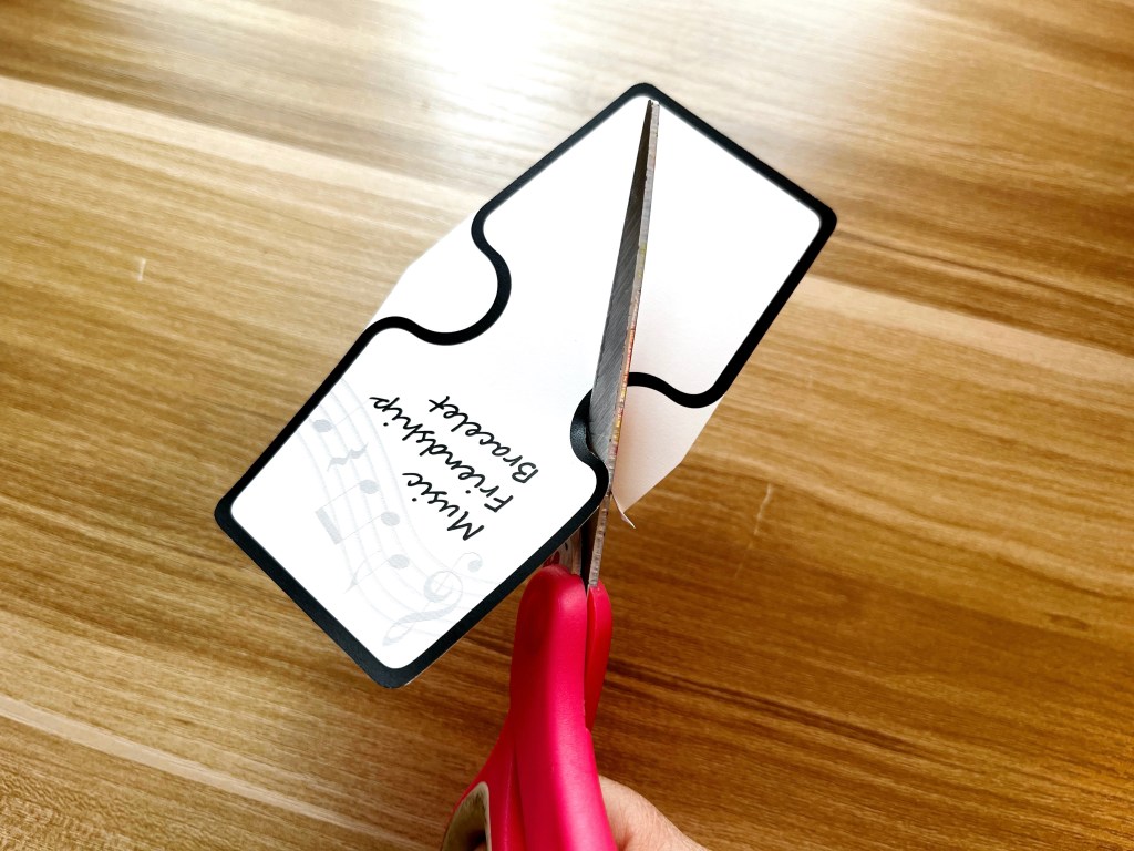 A pair of pink scissors are being used to cut out a bracelet display card.