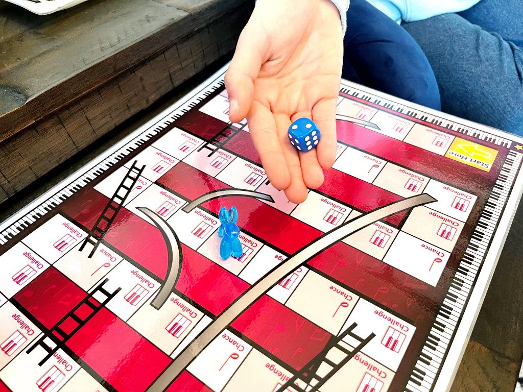 Piano student rolls a blue die while playing the recital prep game, Slurs and Ladders.