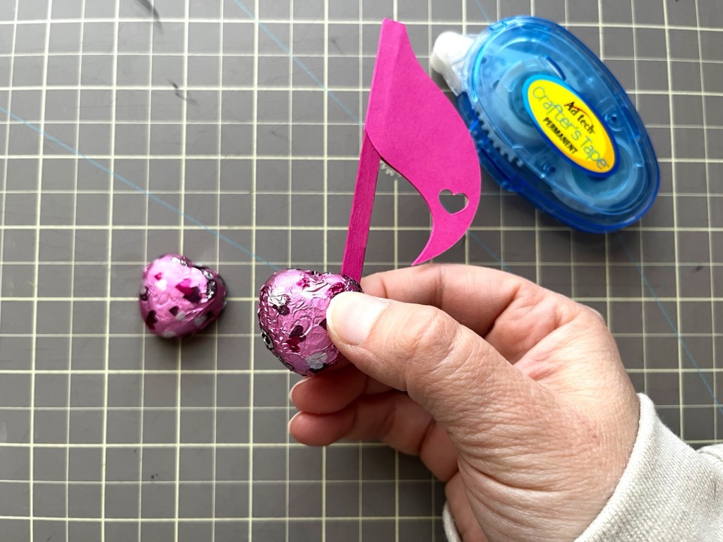 A chocolate is pressed against the tape on the pink eighth note stem