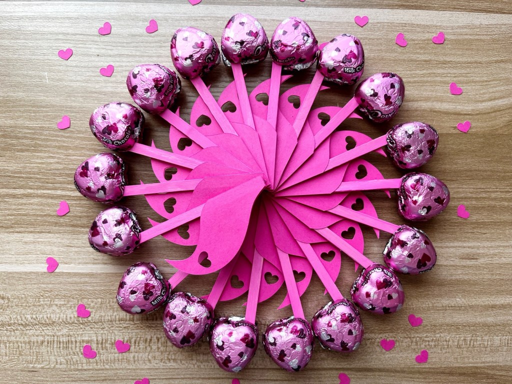 Chocolate eighth notes are arranged in a circle with the flags at the center. The chocolates are surrounded by tiny pink hearts.