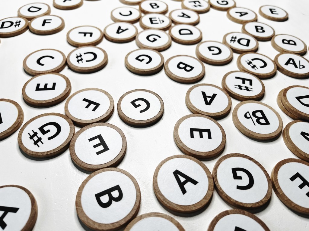 Wood coins with music pitches printed on them are arranged on a white table.