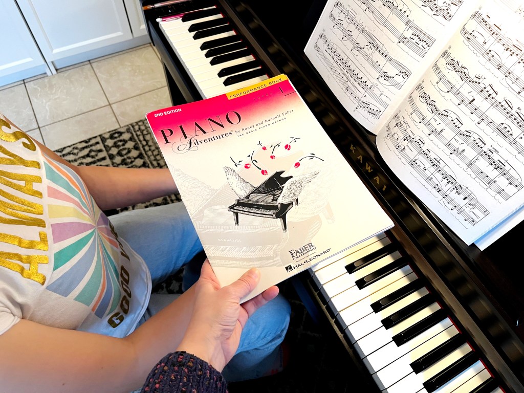 Piano teacher holds a book over a piano students hands to obstruct their view of the keyboard.