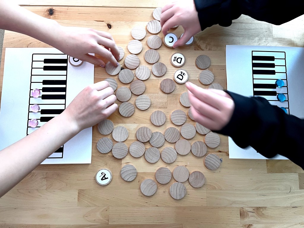 Players quickly turn over the wooden circles at the center of the table to reveal the pitches and attempt to find an A, a C, and an E.