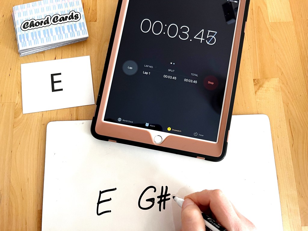 A piano student quickly writes down the notes of an E major chord as a stopwatch times them to see how long it takes.