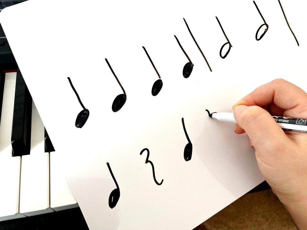 A piano teacher writes out a rhythm sequences of quarter notes, quarter rest, and half notes on a dry erase board.