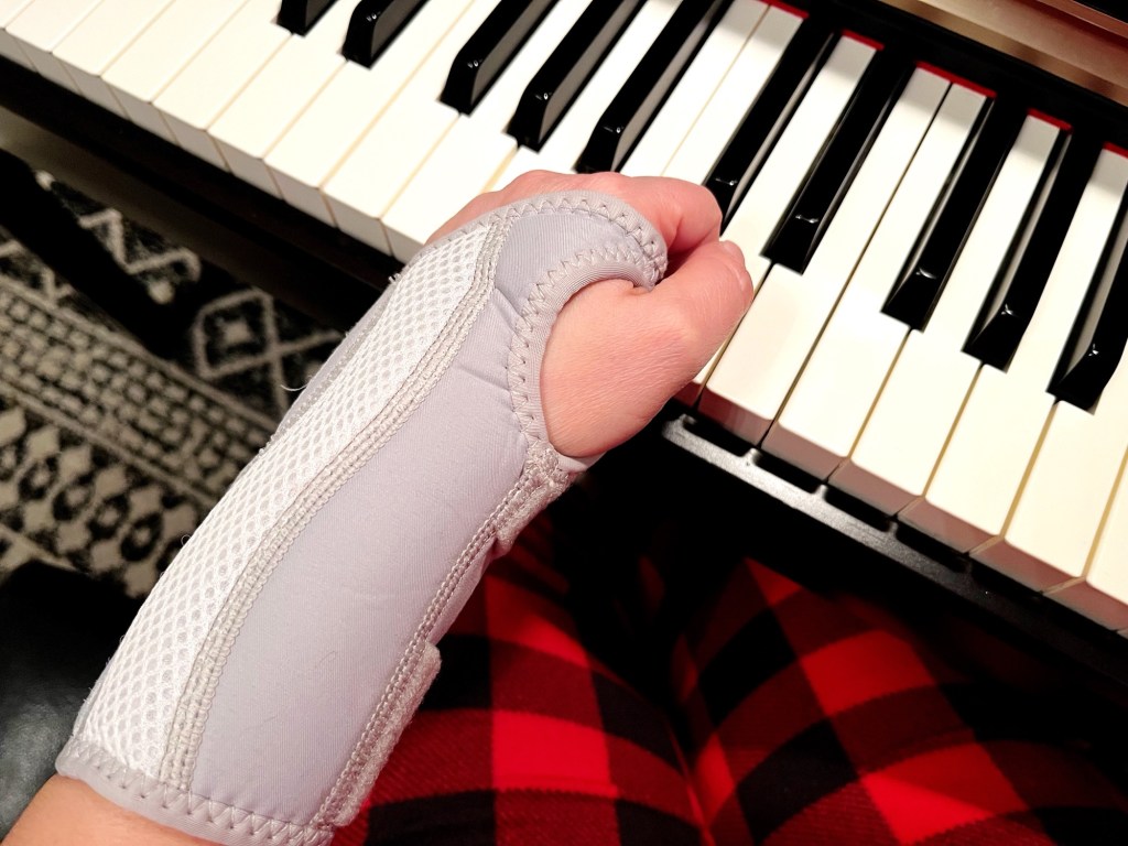 A hand in a wrist brace sits on the keys of a piano
