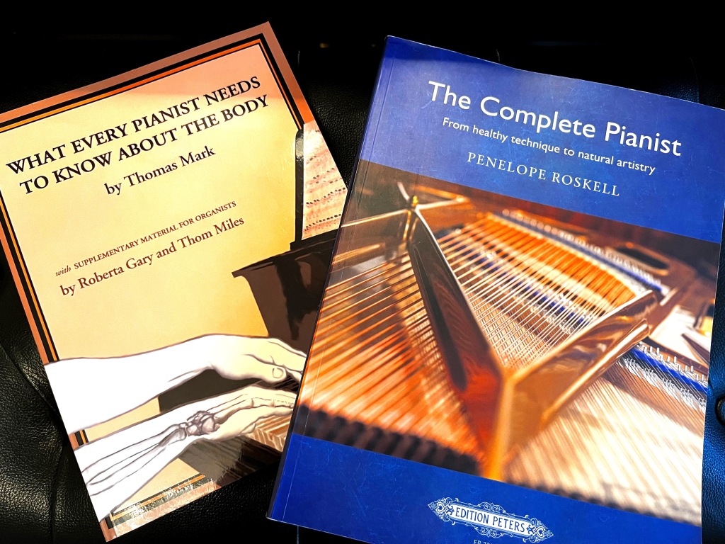 Two books about body mechanics and piano playing sit on top of a piano bench.