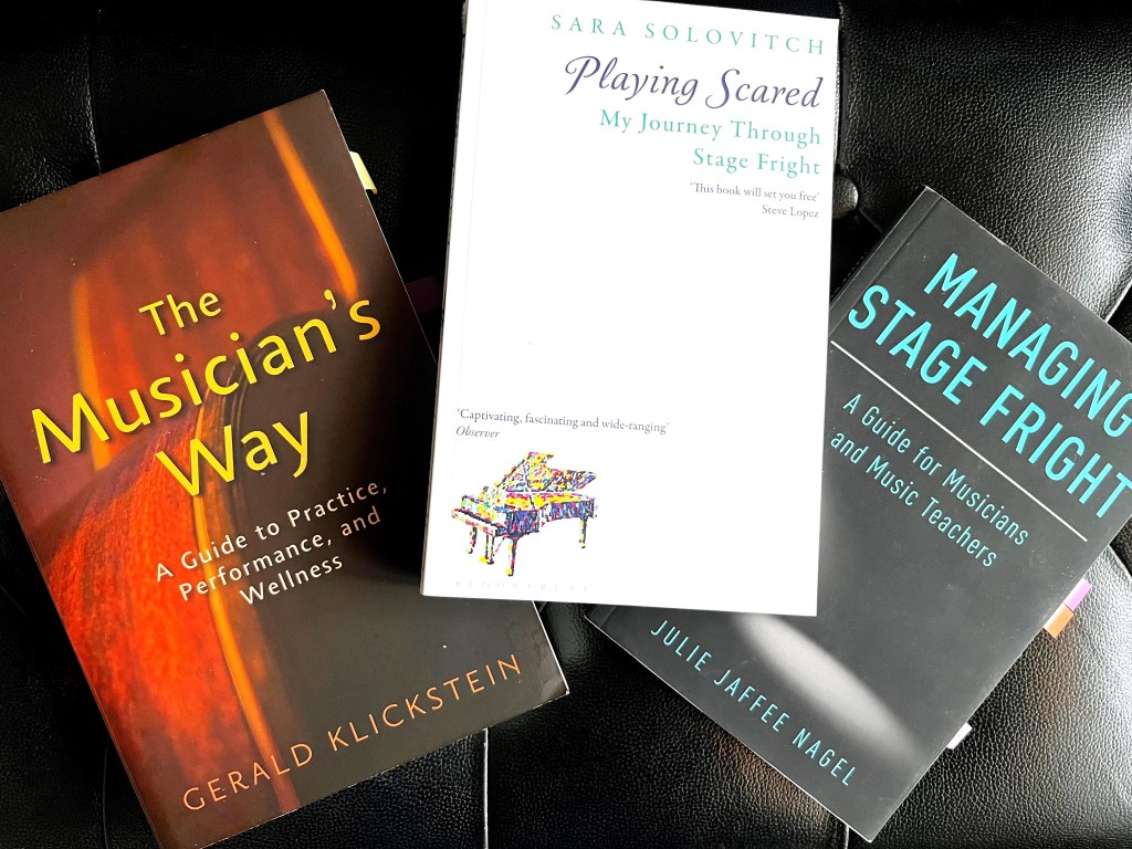 Three books lay on a piano bench: The Musician's Way, Playing Scared, and Managing Stage Fright.