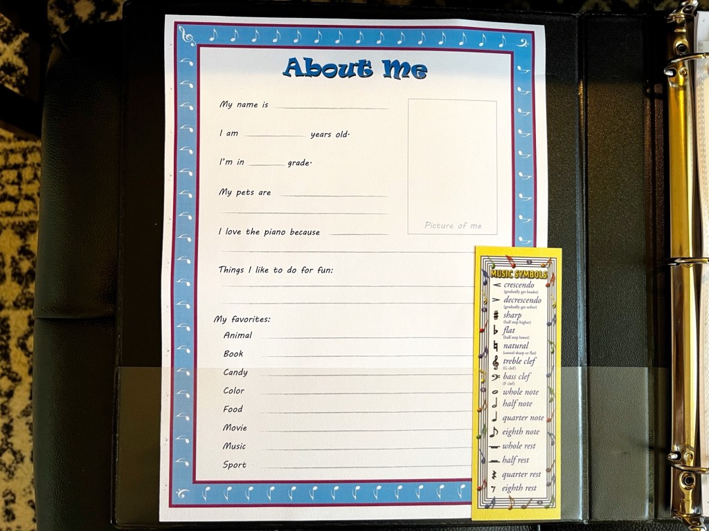 A binder is open and it’s front cover holds a print out entitled “About Me”as well as music theory bookmark in its front pocket.